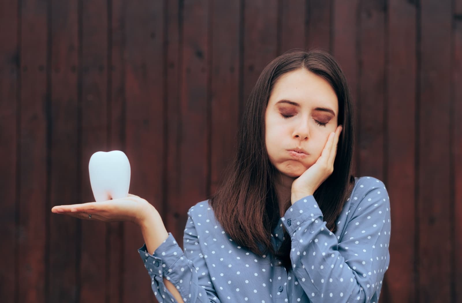 An unhappy person holds a large model of a tooth while resting their hand on their painful jaw.