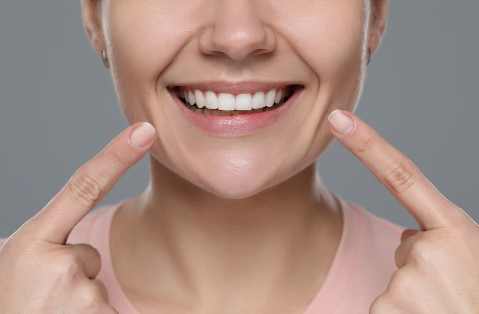 A person points at their healthy smile after recovering from wisdom teeth removal.