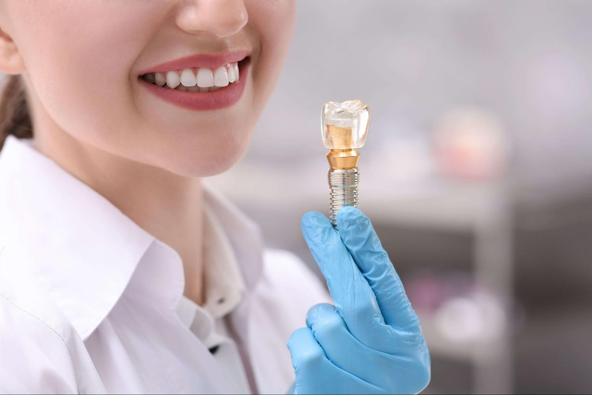 A dentist holds up s model of the dental implant, which shows the small screw and crown that are being held on by the abutment.